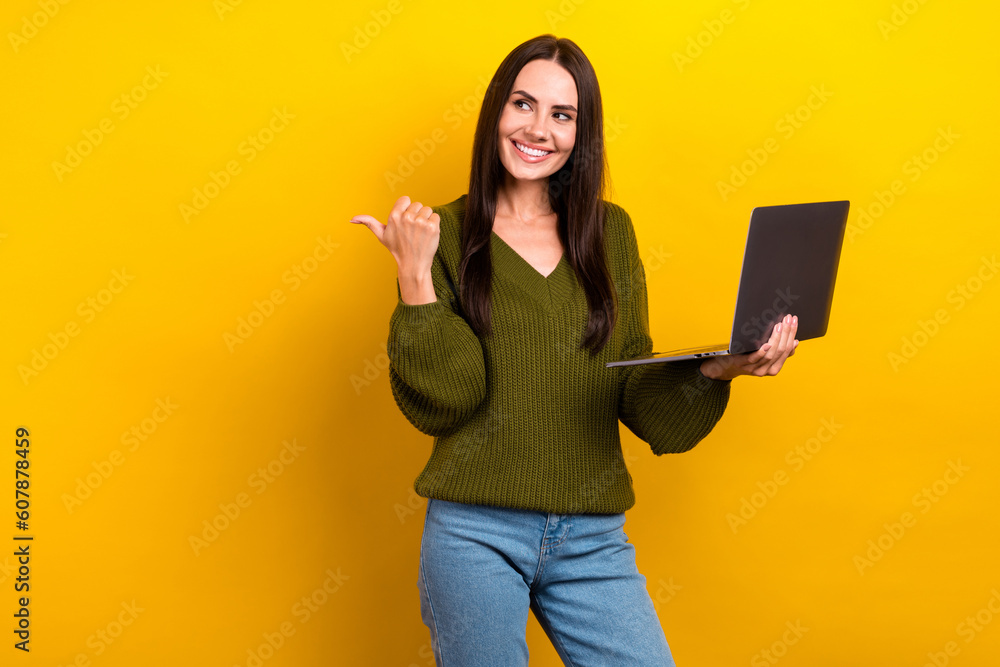 Photo of cheerful charming lady hold netbook look indicate finger empty space isolated on yellow color background Photo of cheerful charming lady hold netbook look indicate finger empty space isolated on yellow color background
