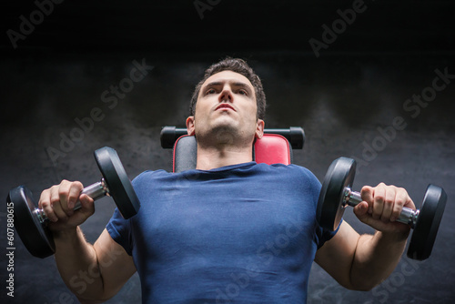 Handsome weightlifter lifting bench press working out with dumbbell in the gym