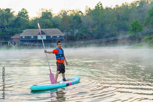 man on Paddleboard or sup board in middle of lake and enjoying sunrise and fog in the morning