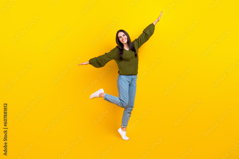Full size photo of overjoyed nice girl stand one leg arms wings good mood isolated on yellow color background Full size photo of overjoyed nice girl stand one leg arms wings good mood isolated on yellow color background