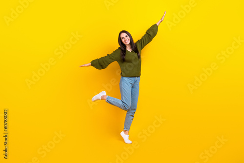 Full size photo of overjoyed nice girl stand one leg arms wings good mood isolated on yellow color background