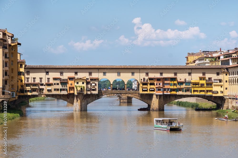 Ponte Vecchio bridge over the Arno river with a touristic boat daytime photo in old Florence city, Toscana, Italy. Old architectural construction is unique and most visited attractive tourists sight.