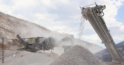 Stone crushing machine at open pit mining and processing plant for crushed stone. Piles of gravel stone and conveyor belts on the side of the road, slow motion