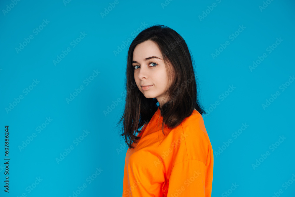 Fototapeta premium Stunning Young Woman in Trendy Orange Outfit Poses for Portrait, Isolated on Blue Background, Lovely Model with a Captivating Gaze and Gorgeous Appearance