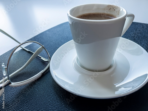 White cup with black coffee and glasses on the table