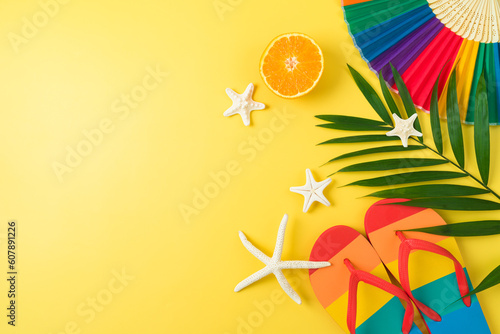 LGBTQ pride month beach party concept with rainbow flip flops palm leaf and  paper fan on yellow background. Top view, flat lay