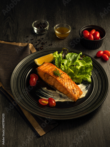 Grilled or fried salmon steak and green salad, lemon, tomato, sauce, side dish. Healthy traditional seafood with cooked fish