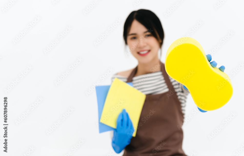 Young smiling happy housekeeper woman wear brown apron and blue rubber gloves hold in hand sponge and wipes. isolated on white background studio. Housework concept Young smiling happy housekeeper woman wear brown apron and blue rubber gloves hold in hand sponge and wipes. isolated on white background studio. Housework concept