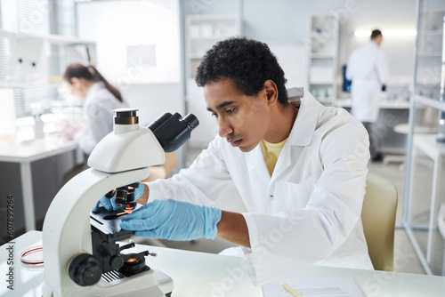 Portrait of ethnic young scientist setting up electronic microscope in laboratory  copy space
