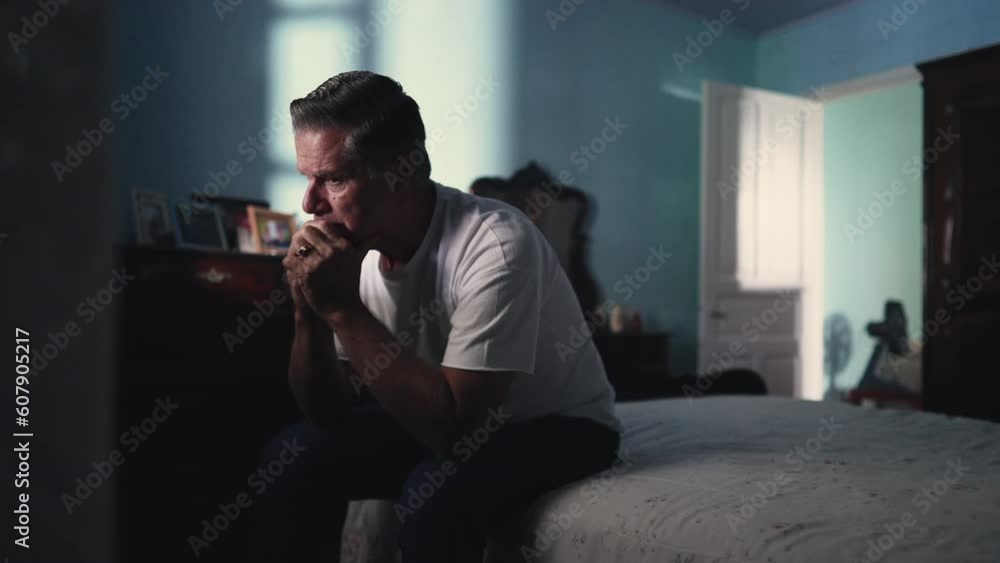 Contemplative older man sitting by bed pondering problems. Person in 50s dwelling with life's difficulties. Loneliness and solitude concept in middle age suffering from abandonment Contemplative older man sitting by bed pondering problems. Person in 50s dwelling with life's difficulties. Loneliness and solitude concept in middle age suffering from abandonment