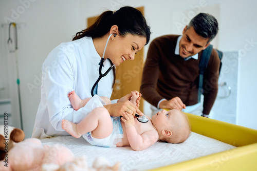 Happy pediatrician using stethoscope during baby's check up at medical clinic.