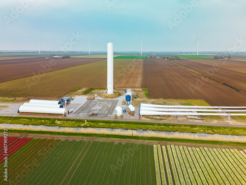A construction site of a new windmill surrounded by tulip fields and a canal in holland on a spring day