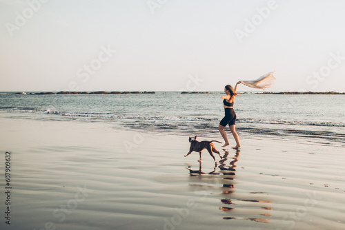woman running in the wind with her dog on the beach