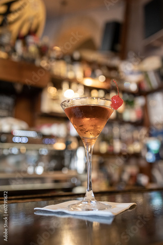 Warm  cozy bar interiors. Close up shot of a beautiful brown liqueur or drink in a martini glass  with a sweet red candied cherry on the edge of the glass. Adult relax.