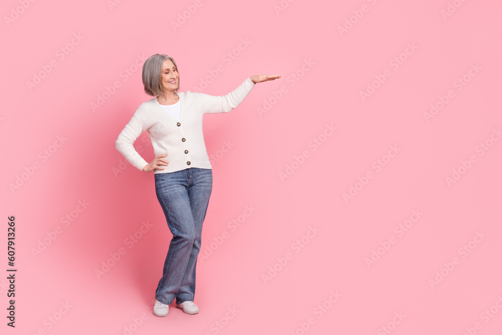 Full body portrait of cheerful aged lady arm demonstrate measure height empty space isolated on pink color background Full body portrait of cheerful aged lady arm demonstrate measure height empty space isolated on pink color background