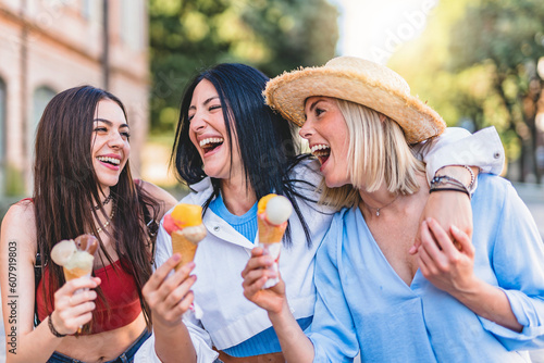 Group of happy young women eating ice cream outdoors at urban city place- Three cheerful friends girls having fun and walking together at city enjoying summer- Joyful Friendship Lifestyle Concept 