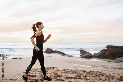 Cheerful slim adult european lady in sportswear race walking, enjoys workout in morning on sea beach