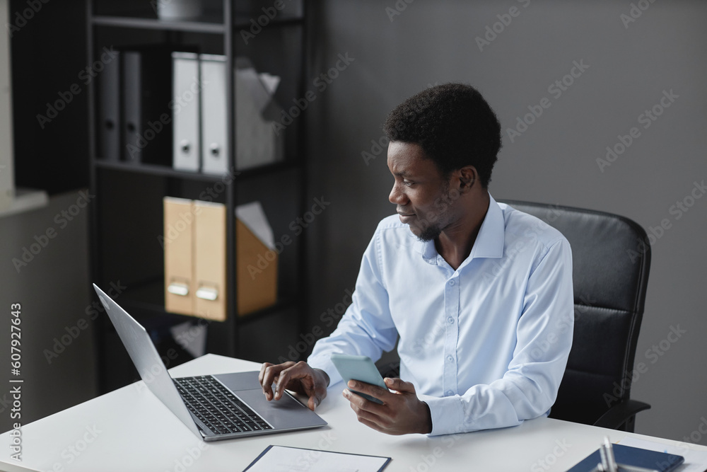 High angle portrait of young black businessman using laptop while sitting at workplace desk in office, copy space High angle portrait of young black businessman using laptop while sitting at workplace desk in office, copy space