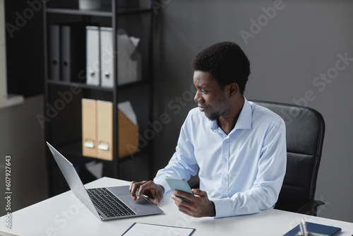 High angle portrait of young black businessman using laptop while sitting at workplace desk in office, copy space
