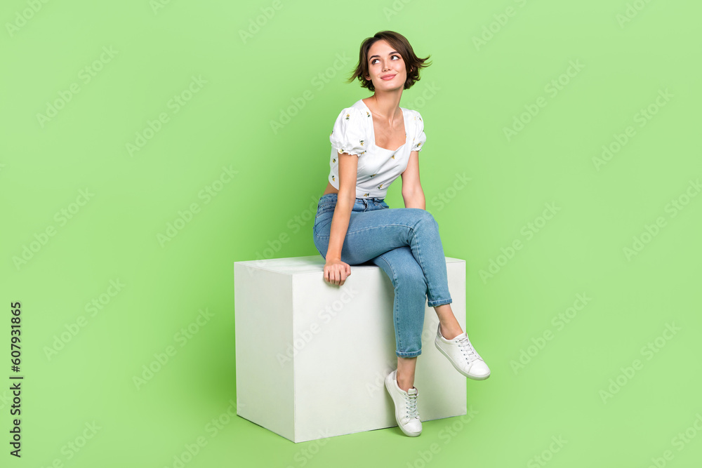 Full length photo of cheerful thoughtful woman dressed white blouse siting podium looking empty space isolated green color background Full length photo of cheerful thoughtful woman dressed white blouse siting podium looking empty space isolated green color background