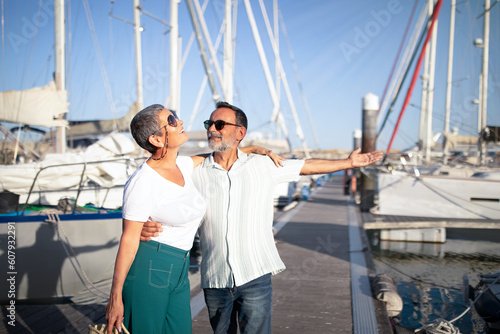 Senior Husband Hugging Wife Showing Their New Yacht In Marina