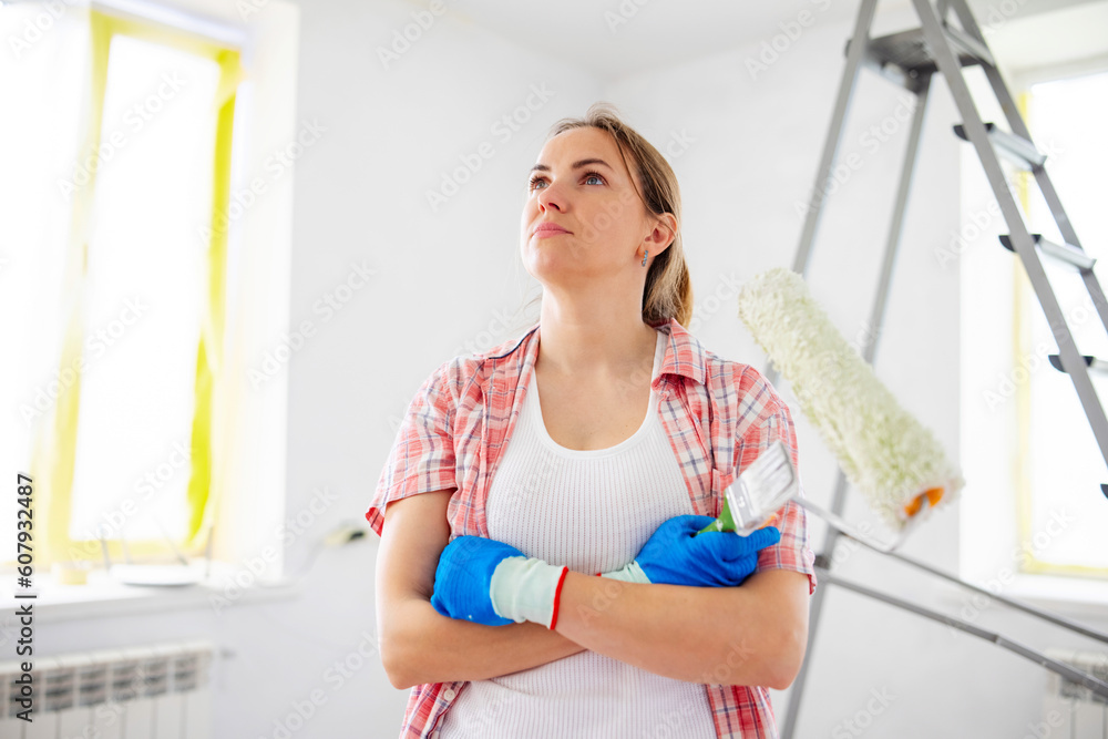 Positive woman holding dirty roller and brush after painting walls in room Positive woman holding dirty roller and brush after painting walls in room