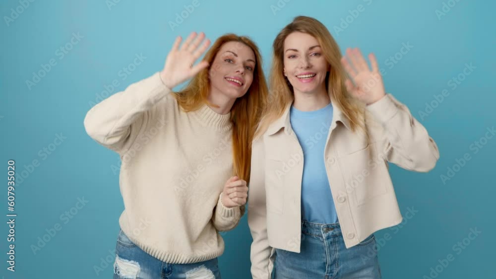 Friends, woman showing hello hi gesture, smiling friendly, greeting and welcome guest. Two women sister, happy surprised emotion. Indoors studio shot stylish lady isolated on blue background. Friends, woman showing hello hi gesture, smiling friendly, greeting and welcome guest. Two women sister, happy surprised emotion. Indoors studio shot stylish lady isolated on blue background.