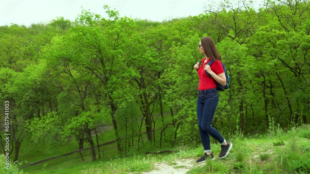 Tourist woman with backpack walking in deciduous forest. Active adult leisure of hiking in green valley. Person enjoy wanderlust and view of the spring grassy hill. Female hiker explore of wildlife. Tourist woman with backpack walking in deciduous forest. Active adult leisure of hiking in green valley. Person enjoy wanderlust and view of the spring grassy hill. Female hiker explore of wildlife.