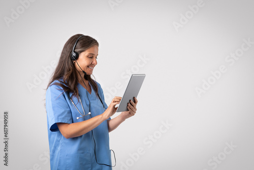 Telemedicine concept. Cheerful senior woman doctor with tablet and headset making online consultation, free space