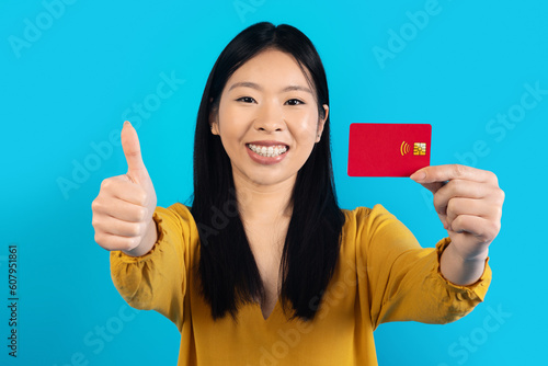 Happy asian lady showing credit card and thumb up © Prostock-studio