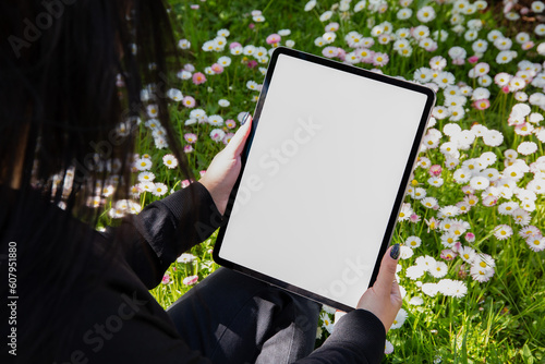 Young woman using Ipad, blank empty mockup screen. in a field of flowers. Women are reading news the garden: Freelance, student lifestyle, drawing, gardening.