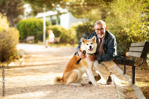 Smiling european old man in casual and glasses enjoy walk with dog and spare time, hugs in park, outdoor photo