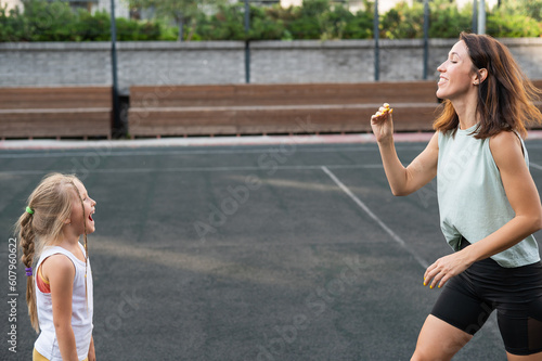 Mom and daughter have fun on the outdoor sports ground. A Caucasian woman throws candy and a girl catches it with her mouth. © Михаил Решетников