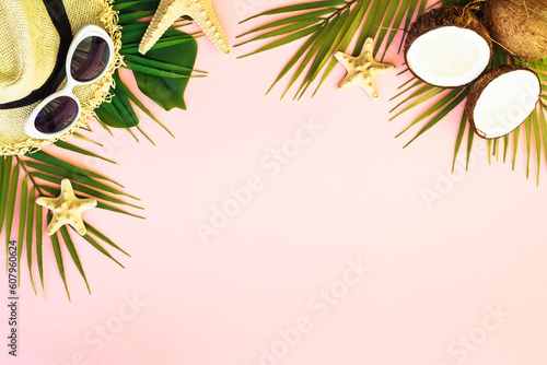 Summer holidays on pink background. Palm leaves, coconut, hat and sea shells on pink background.