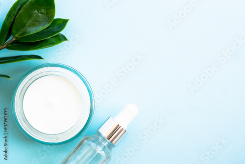 Natural cosmetic, cream jar with green leaves on blue. Flat lay with copy space.