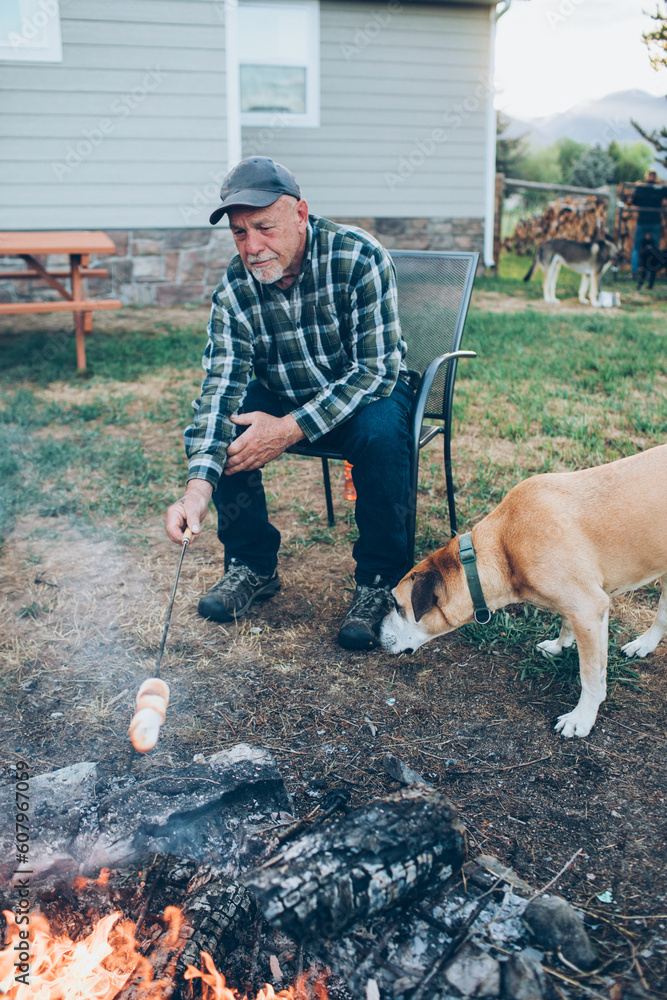man roasting marshmallows over a fire with his dog
