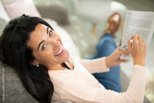 smiling woman holding crossword book on couch photo