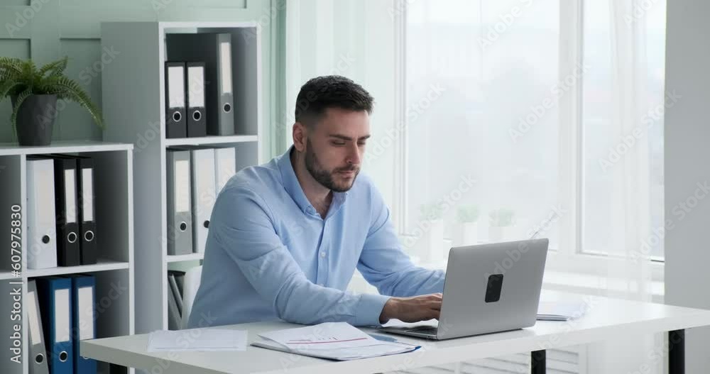 Business executive in shirt sitting at his desk, looking over papers and graphs spread out in front of him. Using his laptop to cross-reference data, he strives to stay ahead of the competition. Business executive in shirt sitting at his desk, looking over papers and graphs spread out in front of him. Using his laptop to cross-reference data, he strives to stay ahead of the competition.