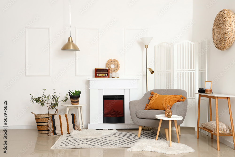 Fototapeta premium Cozy grey armchair with cushion, fireplace and coffee table in interior of living room
