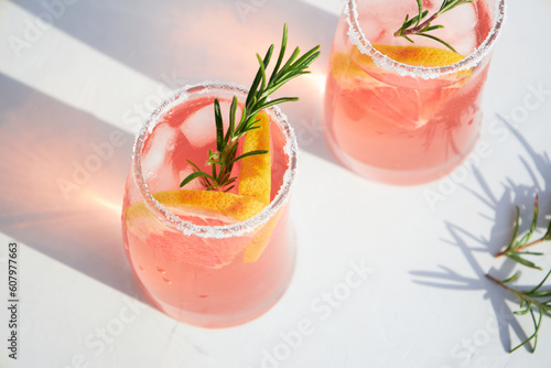 Top view of fresh grapefruit or red orange cocktails, with ice cubes, fresh fruit slices inside and rosemary. Vacation and summer cocktails concept. Citrus drink.
