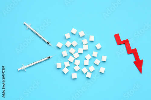 Sugar cubes with syringes for insulin injection and arrow directed downwards on blue background
