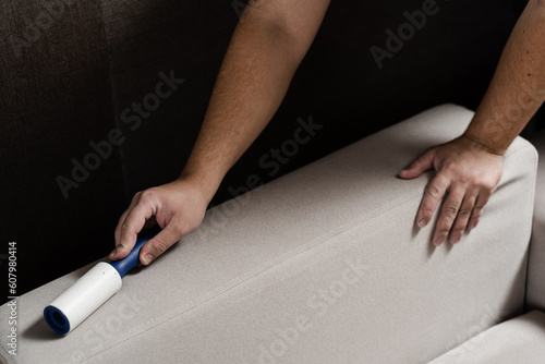 Process of cleaning couch using lint roller from cat and dog hair. Cleaner is removing lint from sofa using cleaning roller close-up.