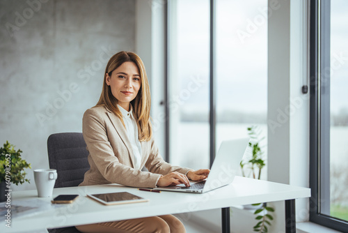 Friendly relaxed young businesswoman leaning against an interior office wall smiling at camera with lateral copy space. Cropped portrait of an attractive young businesswoman standing alone 
