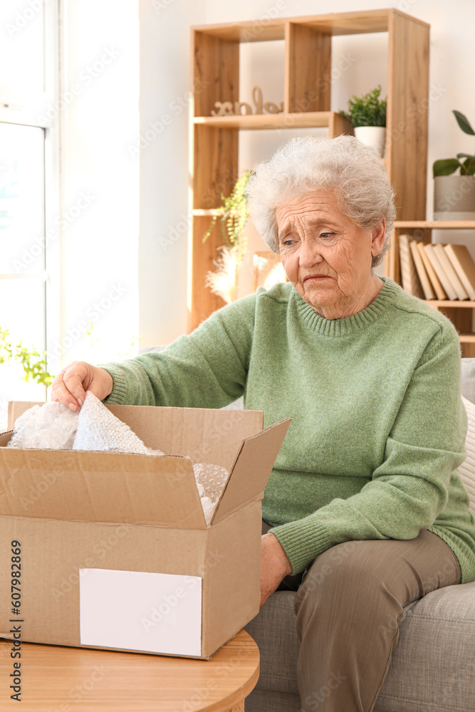Upset senior woman opening parcel at home Upset senior woman opening parcel at home