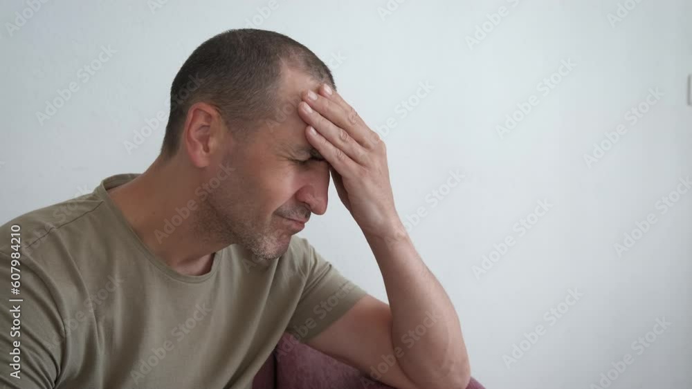 Man experiencing headache at home. An exhausted man sits on the sofa and rubs his temples from headache in the flat. Man experiencing headache at home. An exhausted man sits on the sofa and rubs his temples from headache in the flat.