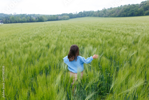 back view of small child in blue sweater running in a vast field of wheat