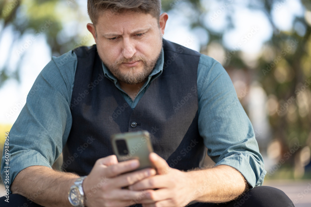 Man sitting in a park using his phone looking intently at the screen