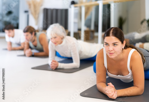 Sporty women and men practicing yoga positions during group training in fitness center, performing stretching asana Urdhva Mukha Shvanasana