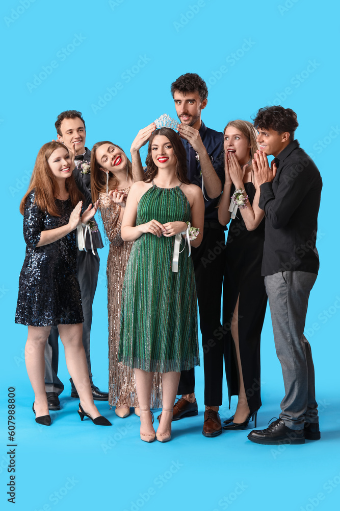 Fototapeta premium Young people crowning prom queen on blue background