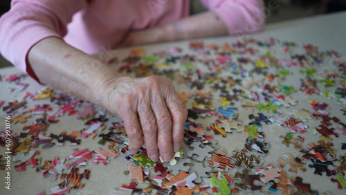 Closeup of elderly old womans hands organizing puzzle pieces on a table.